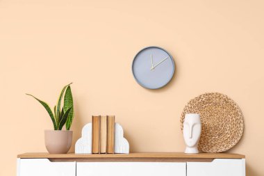 Odadaki bej duvarda kitap ve saat dolu çekmeceler.