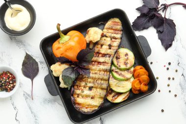 Beyaz arka planda ızgara sebzeli fırın ve fesleğen.