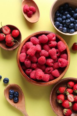 Sarı arka planda taze ahududu, yaban mersini ve çilek kaseleri