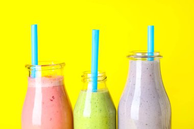 Sarı arka planda farklı taze smoothie şişeleri, yakın plan
