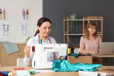 Atölyedeki masada kadın terzi dikiş dikiyor.