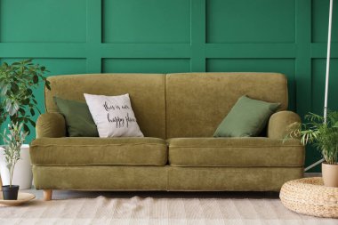 Yeşil duvarın yanında yastıklı ve çiçekli rahat bir kanepe.