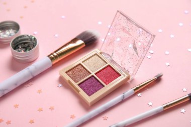 Parıltı kavanozu, konfeti, göz falı paleti ve pembe arka planda makyaj fırçaları ile kompozisyon, yakın plan