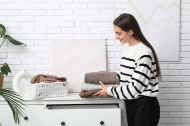 Genç bir kadın evdeki çekmeceye bir yığın kalın kazak koyuyor.