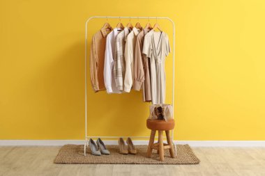 Soyunma odasındaki sarı duvarın yanında giysiler ve ayakkabılar var.