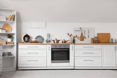 Mutfağın içinde beyaz tezgah, raf ünitesi ve çatal bıçak takımı var.