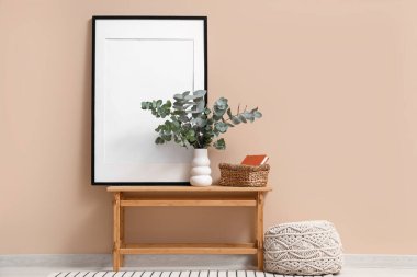 Sepet, fotoğraf çerçevesi ve okaliptüs dallı vazo odada bej duvarın yanında.