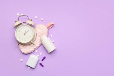 Uyku maskeli çalar saat, haplar ve mor arka planda kulak tıkaçları. Melatonin kavramı