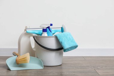 Beyaz duvara karşı lamine zemin üzerinde temizlik ürünleri ve faraş dolu kova
