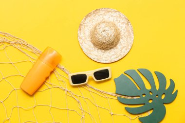 Güneş kremi, güneş gözlüğü ve sarı arka planda ağ olan hasır şapka. Yaz konsepti