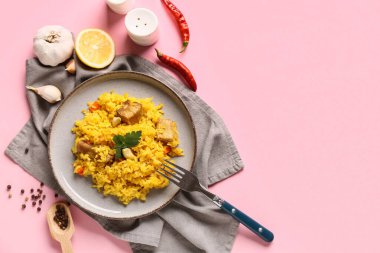 Plate with tasty pilaf and different spices on pink background