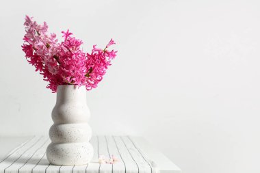 Beyaz duvarın yanındaki masada, üzerinde pembe sümbül çiçekleri olan vazo.