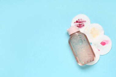 Mavi arka planda bir şişe mikiler suyu ve kirli pamuk pedlerle yakın plan kompozisyonu.