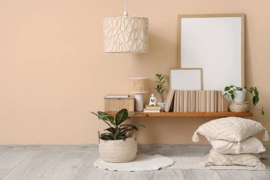 Ev bitkisi, fotoğraf çerçeveleri ve odanın içindeki bej duvarın yanındaki bankta duran kitaplar.