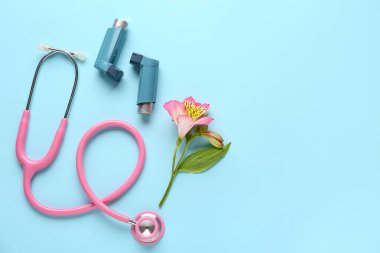 Steteskoplu astım spreyleri ve mavi arka planda alstroemeria çiçeği.