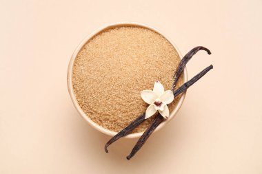 Bowl of vanilla sugar with pods and flower on beige background