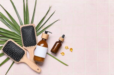 Composition with hair brushes, capsules and bottles of cosmetic products on pink tile background