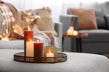Farklı yanan mumlarla dolu bir tepsi ve oturma odasındaki koltukta bir fincan çay, yakın çekim.