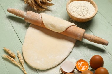 Çiğ hamur, bir kase un, merdane, buğday dikenleri ve yeşil ahşap arka planda yumurtalar.