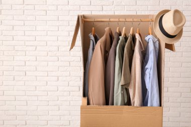 Beyaz tuğla duvarın yanında erkek kıyafetleri ve şapkası olan bir gardırop.