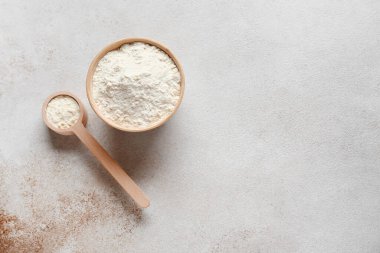Bowl of powdered milk with wooden measuring scoop on grunge background