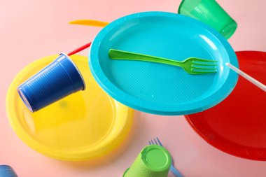 Flying colorful plastic tableware on pink background, closeup