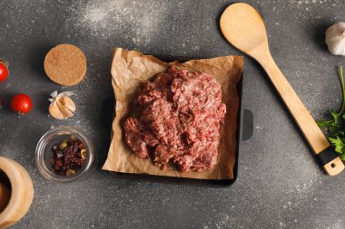 Taze et, sarımsak, domates ve gri grunge arka planda ahşap spatulayla pişirme kabı.