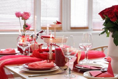 Güllü şenlik masası, yemek odasında yanan mumlar ve bardaklar, yakın çekim. Sevgililer Günü kutlaması