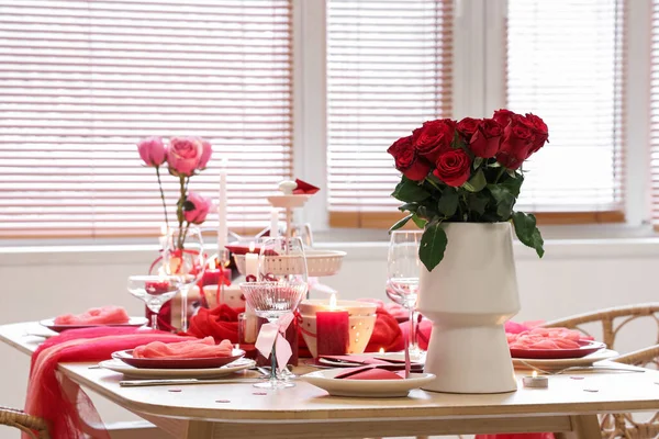 Güllü şenlik masası, yemek odasında yanan mumlar ve bardaklar, yakın çekim. Sevgililer Günü kutlaması