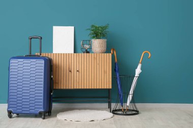 Ahşap dolapta mavi duvarın yanında dekor ve bavul var.