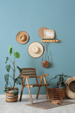 Odanın içinde ahşap sandalye, ev bitkileri, hasır sepet ve mavi duvardaki raf.