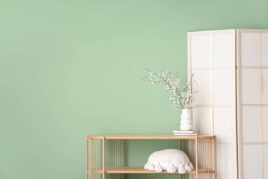 Katlanan ekran ve çiçek açan ağaç dalları yeşil duvarın yanındaki ahşap masada.