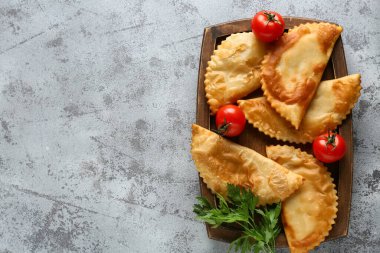 Gri grunge masasında lezzetli chebureks, domates ve maydanoz.