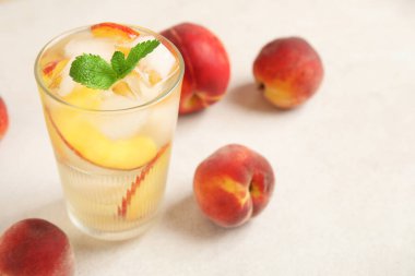 Şeftali dilimleri, buz küpleri ve beyaz arka planda nane yapraklarıyla bir bardak içki.