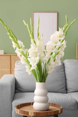 Oturma odasının iç tarafındaki masada güzel beyaz gladiolus çiçekleri olan vazo, yakın plan.