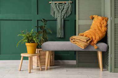Güzel odadaki yeşil duvarın yanında rahat bir bank, ev bitkisi, yastık ve ekose.