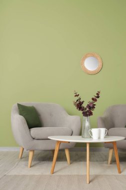 Oturma odasının içinde ayna, gri koltuklar ve masa var.