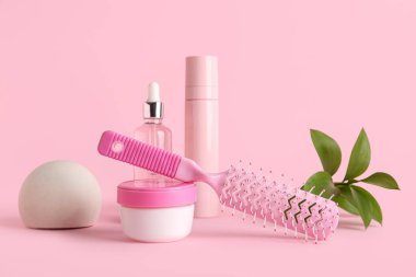 Saç fırçası, kozmetik ürünleri ve pembe arka planda bitki dalı olan kompozisyon