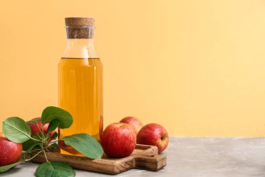 Bir şişe taze elma şarabı ve gri masada meyveler.