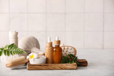 Tepsisi, bitkisel poşetleri, gri grunge masasında kozmetik ürünleri olan spa kompozisyonu, karo duvarın yanında, yakın plan.