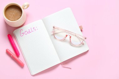 Listesi boş bir defter, pembe arka planda gözlük ve bir fincan kahve. Yeni yıl hedefleri