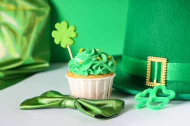 Lezzetli kek, leprikon şapkalı ve papyonlu Aziz Patrick Günü için yeşil arka planda beyaz masada.