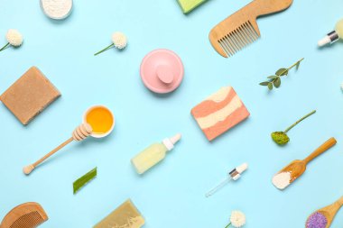 Saç derisi masaj aletleri, şampuanlar, farklı cilt ürünleri ve mavi arka planda çiçekler.