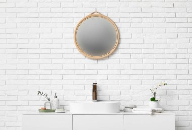 Banyodaki beyaz tuğla duvarın yanındaki tezgahta banyo malzemeleri ve güzel çiçeklerle modern lavabo.