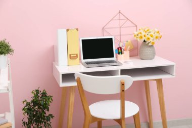 Bir buket narsisli çiçek, kırtasiye ve dizüstü bilgisayarlı iş yeri şık bir ofiste pembe duvarın yanında.