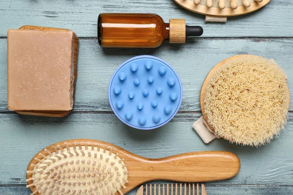 Saç derisi masaj aleti, şampuan çubukları, fırçalar ve mavi ahşap arka planda kozmetik yağı.