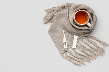 Termometreyle hızlı grip testi, gri arka planda bir fincan çay ve eşarp.