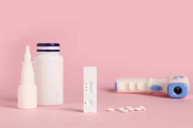 Geniz damlası, kızılötesi termometre ve pembe arka planda haplarla hızlı grip testi.