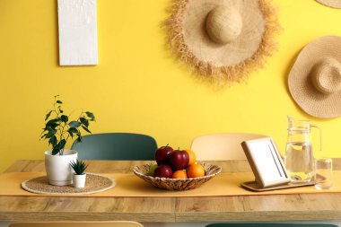 Sarı duvarın yanında sandalyeleri, çiçekleri, suyu ve meyve kasesi olan modern yemek odasının içinde.