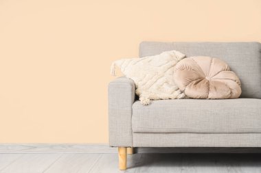 Aydınlık duvarın yanındaki bej koltukta yastıklı şık bir oda.